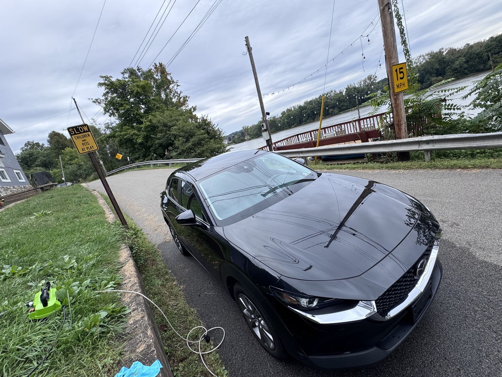 Clean black Mazda parked on a road by the water.