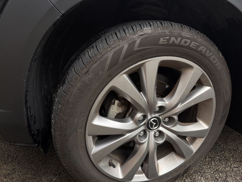 Dusty black Mazda front wheel and fender with dirt on the tire and rim.