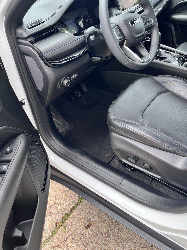 Driver seat, dash and clean front floor mat seen from the open door.